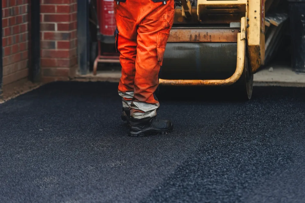 Construction worker operating machinery on freshly laid asphalt in a parking lot project