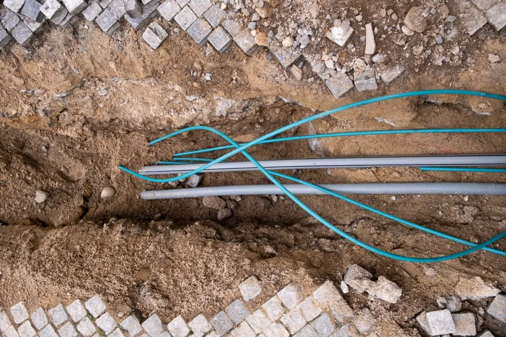 Underground electric cable infrastructure communication installation at a construction site with various cables protected in tubes. High-speed internet network cables are buried underground