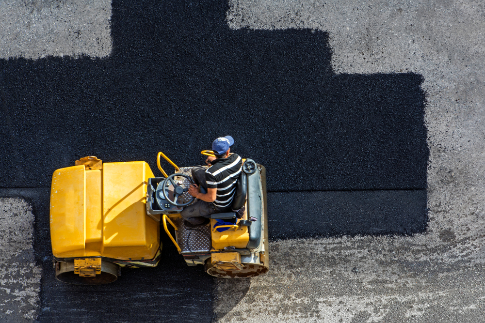 Aerial view of asphalting construction works with commercial repair equipment road parking for the car with yellow roller compactor machine. Contrast between new and old road surface